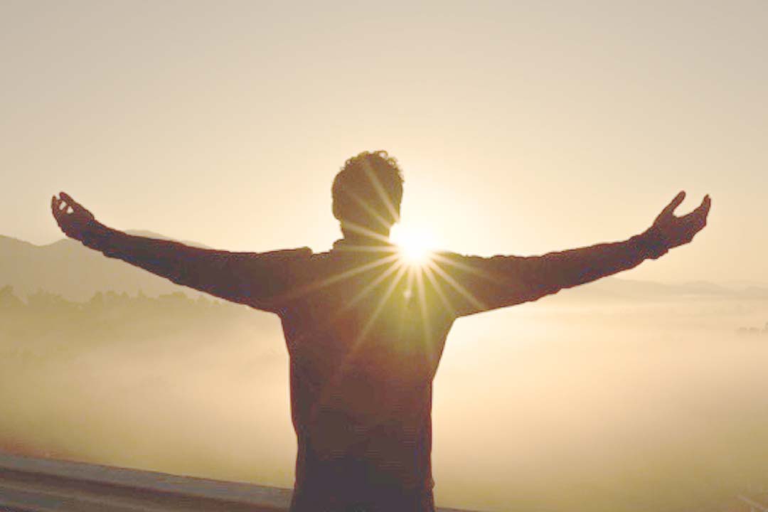 Mann mit ausbgebreiteten Armen vor Sonnenaufgang